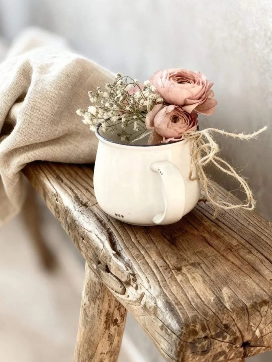 Rustic wood bench with a white mug of pink flowers and neutral linens—lifestyle gift inspiration.