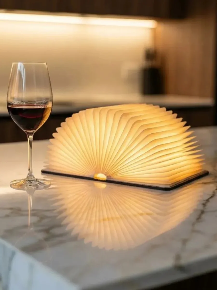 Wooden Book Lamp Review: Affordable Luxury for Your Cozy Home Nook A warm-glowing folding book lamp on a white marble kitchen island next to a glass of red wine.