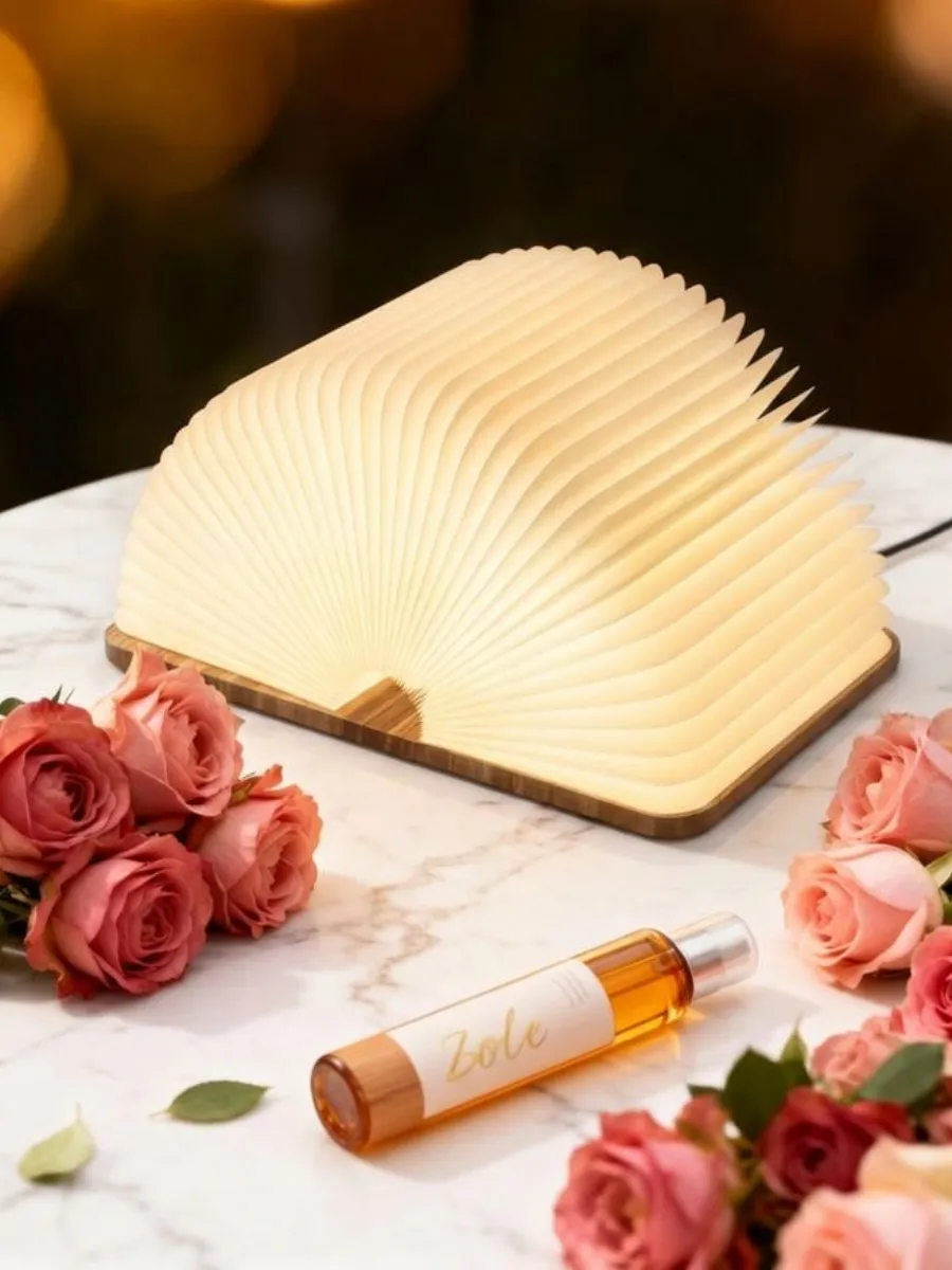 Wooden Book Lamp Review: Affordable Luxury for Your Cozy Home Nook A fanned-open Zbole wooden book lamp glowing on a marble table with pink roses and a Zoe Essentials spray.