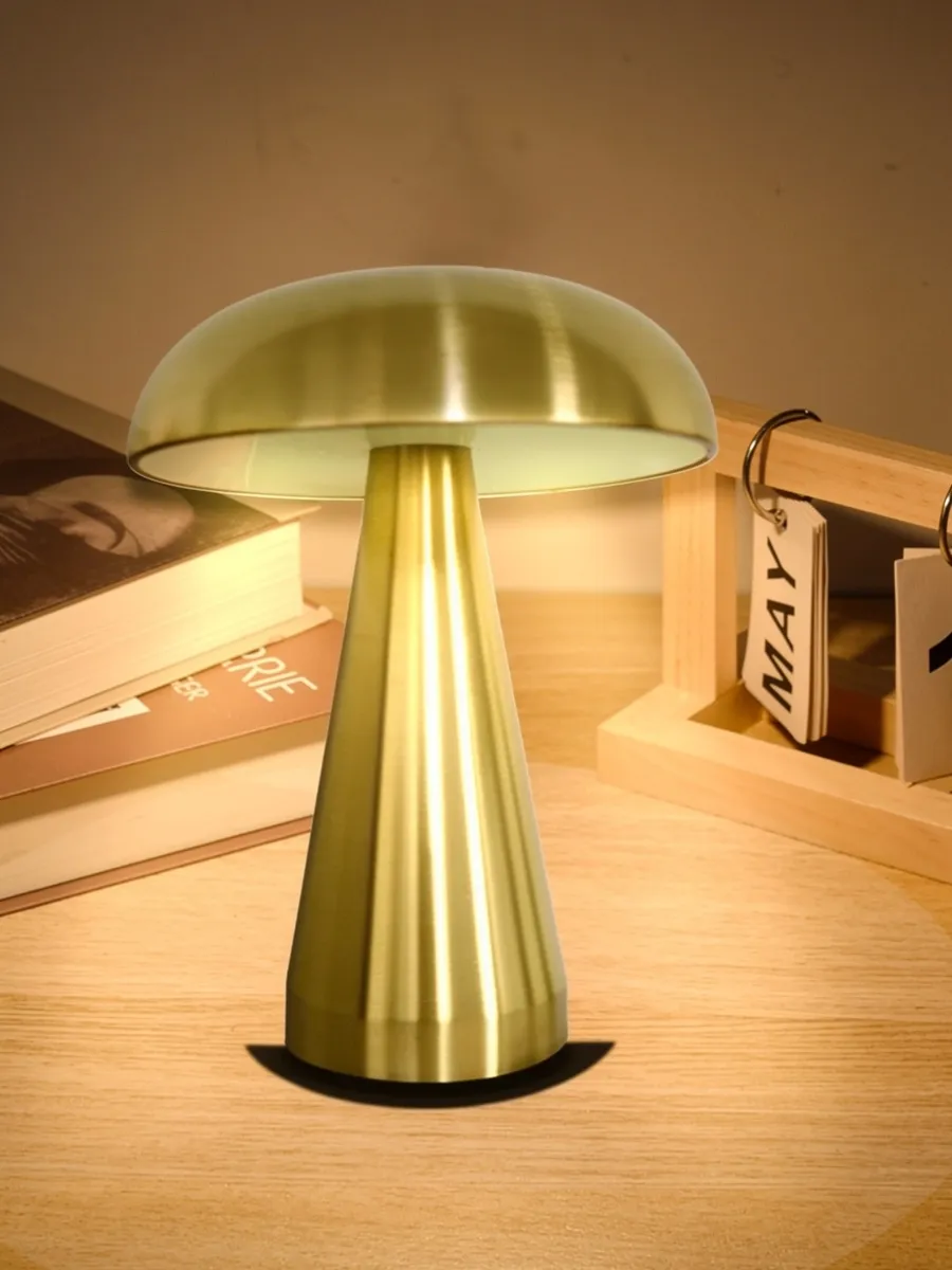 a sleek, cordless mushroom shaped led table lamp in a brushed gold finish, glowing with a soft, warm light on a wooden desk. technical overlay text highlight