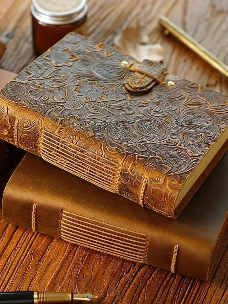 Vintage embossed floral leather journals with hand-stitched binding and a gold fountain pen on a rustic wooden desk.