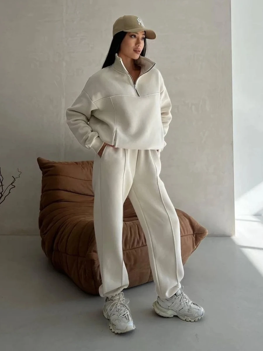 3 Affordable Luxury Spring Capsule 2026 Essentials for a 3-3-3 Wardrobe Woman wearing a cream two-piece lounge set with wide-leg pants and a half-zip sweatshirt, styled with white sneakers and a tan baseball cap for an effortless 2026 airport outfit aesthetic.
