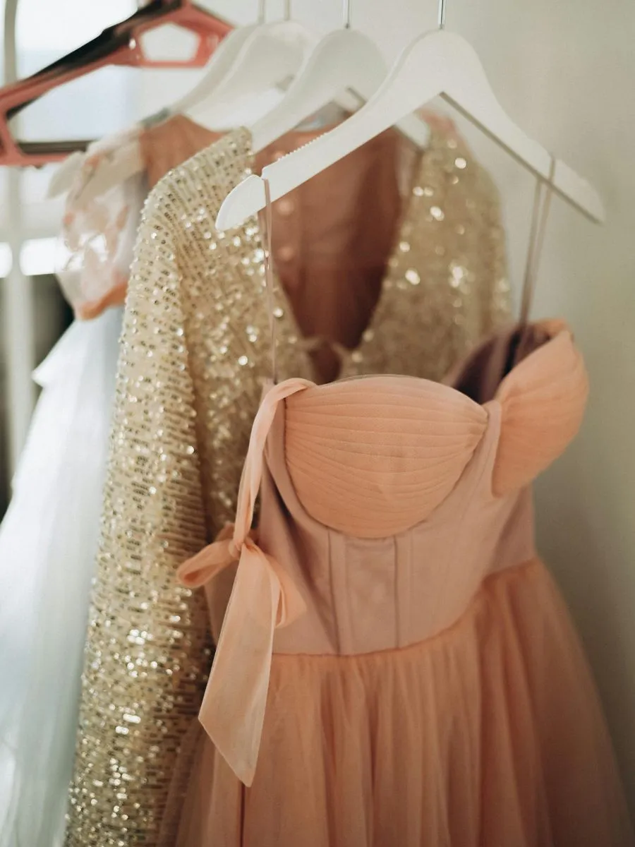 A high-end wardrobe layout showing elegant pink and mauve formal midi dresses hanging safely on natural wood hangers.
