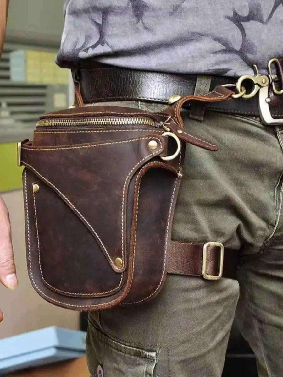 A rugged brown leather thigh fanny pack with a motorcycle leg strap harness and brass zipper hardware.