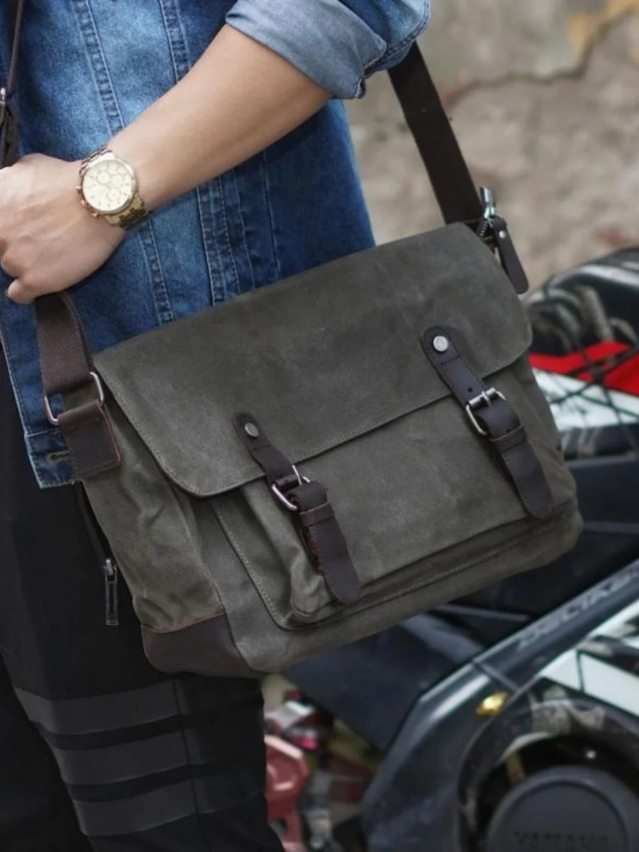 A man wearing a denim shirt and carrying an army green waterproof waxed canvas crossbody messenger bag with dark brown leather straps.