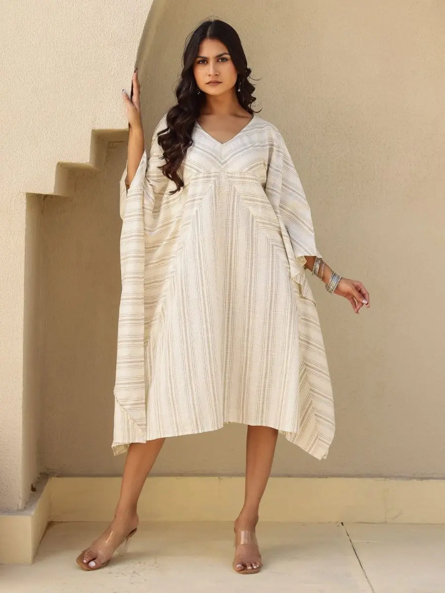 A knee-length natural beige cotton kaftan dress featuring subtle gold vertical stripes and angled panels at the bust.