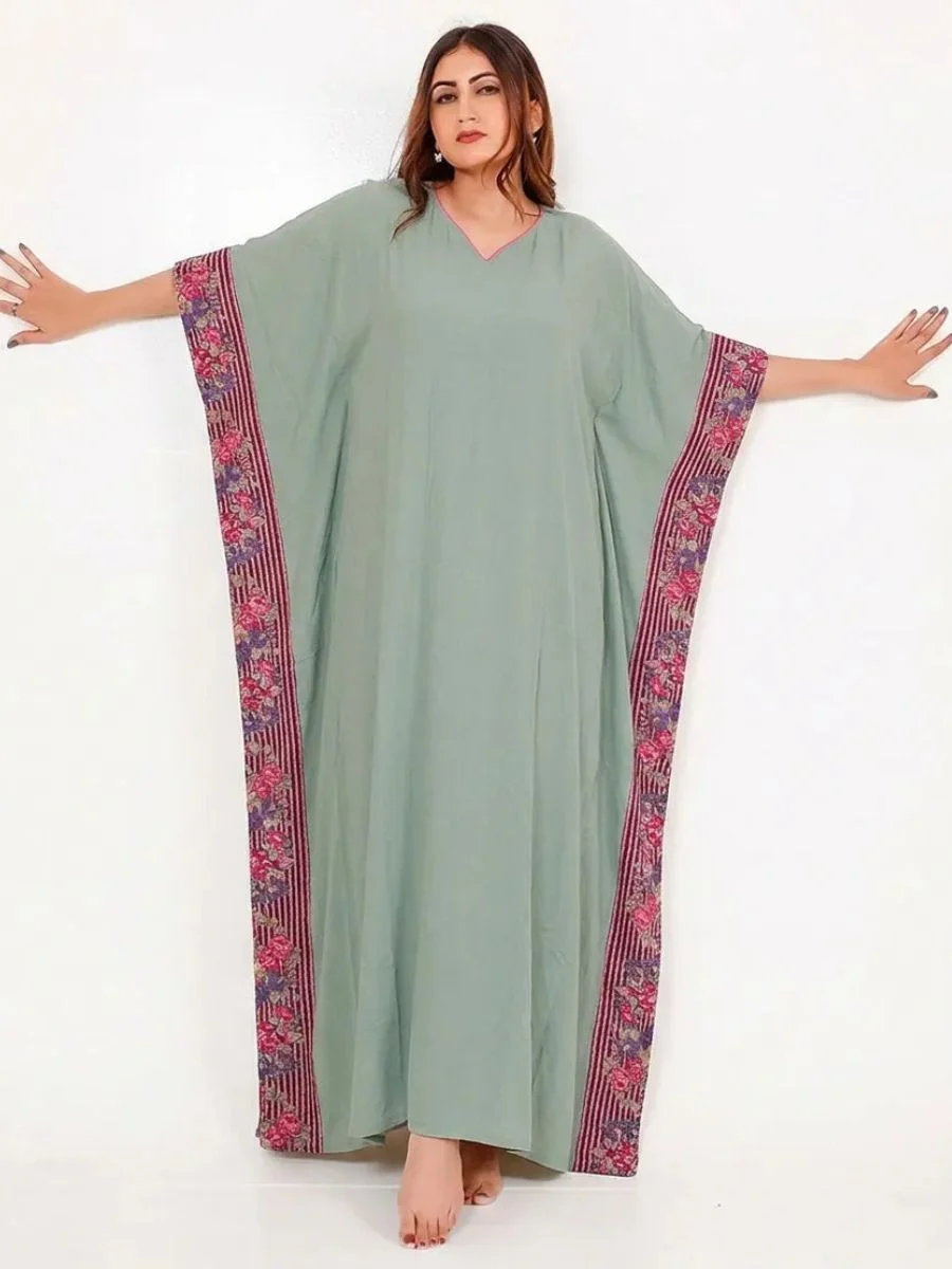 A floor-length sage green viscose twill kaftan dress with bold burgundy and violet floral borders on wide batwing sleeves.