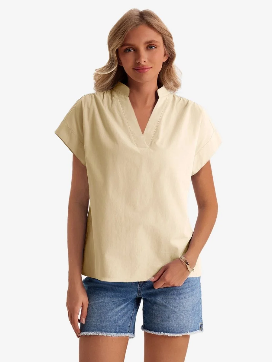 Front view of a woman wearing a light khaki stand collar v-neck blouse with denim shorts.