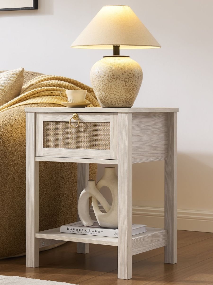 The Terra Nightstand with 1 Drawer in cream oak showing a styled open lower shelf with a geometric ceramic sculpture under an illuminated stone-textured table lamp.