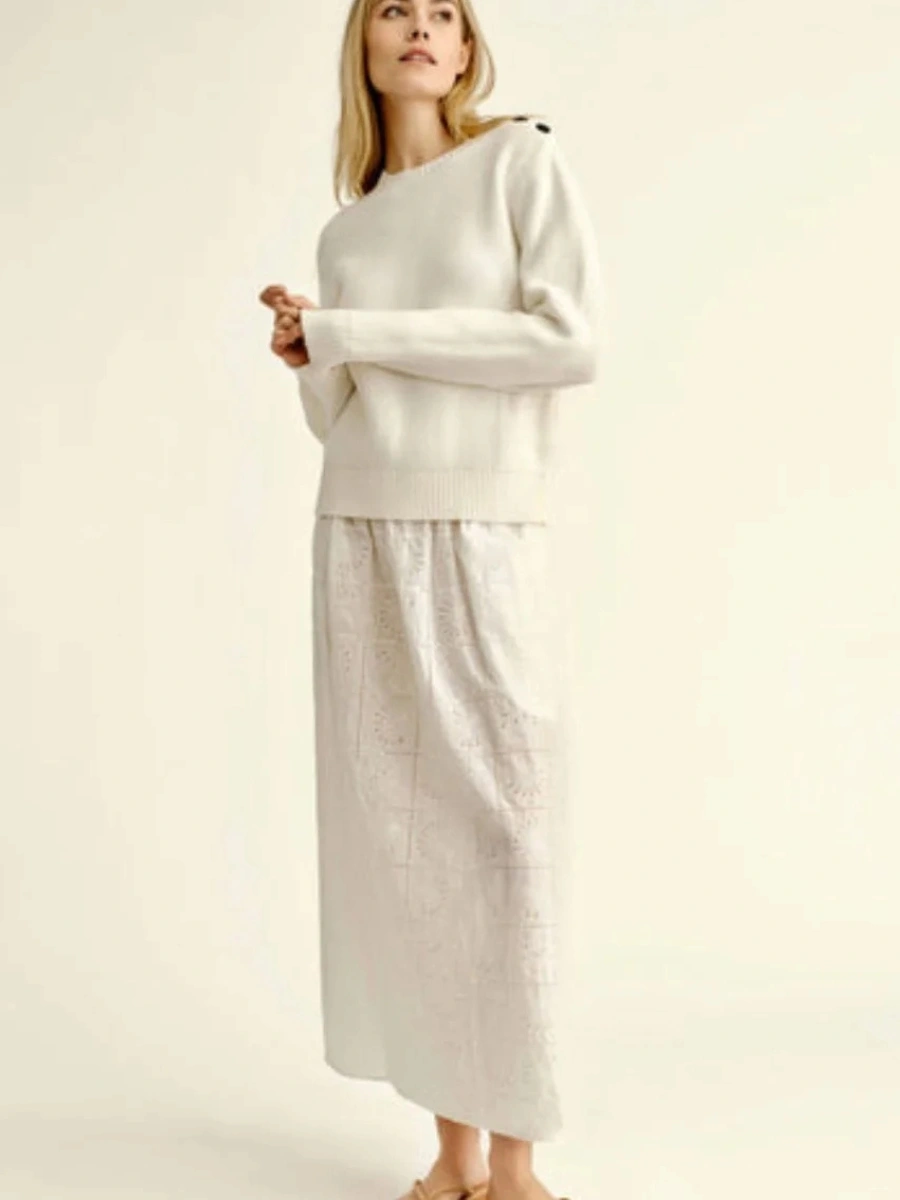 A woman wearing a soft white long-sleeved knit sweater paired with a matching white embroidered eyelet maxi skirt for a texture-rich all white outfit.