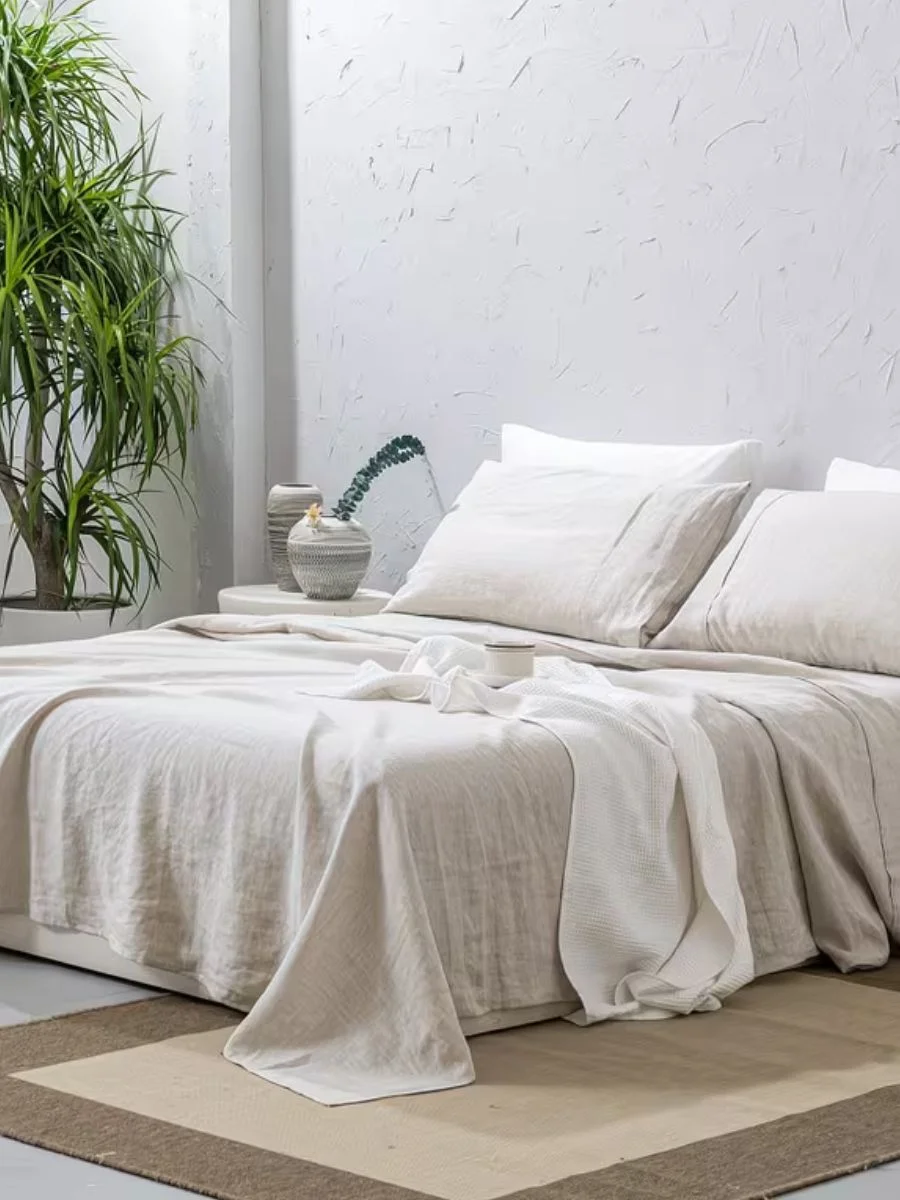 A neutral beige 100% French flax linen sheet set on a low bed with matching pillowcases in a minimalist bedroom.