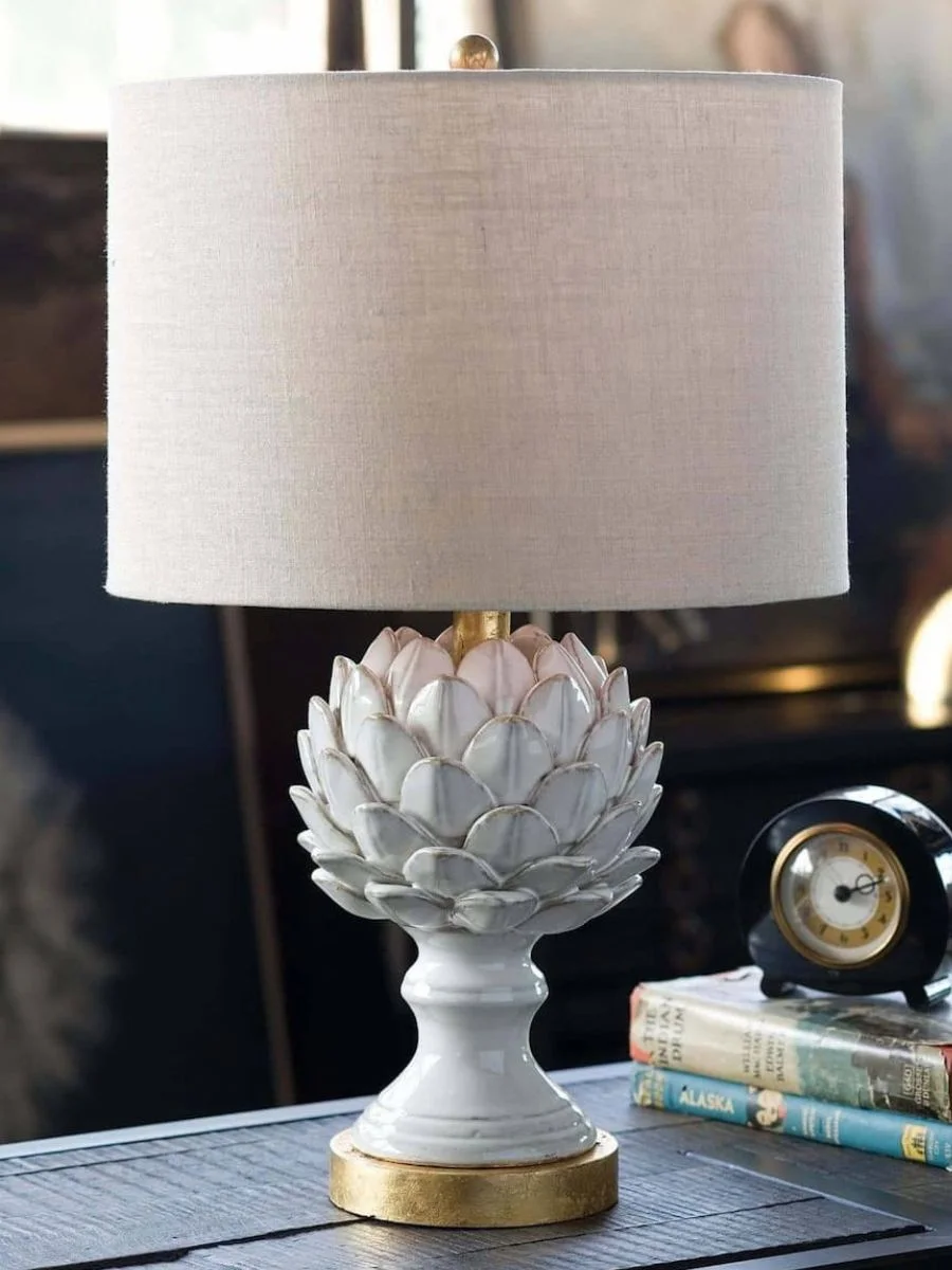 7 Layered Lighting Looks: How to Style Elegant Wall Sconces and Lamps Regina Andrew Leafy Artichoke Ceramic Table Lamp with a textured oatmeal shade sitting on a black console table next to books.