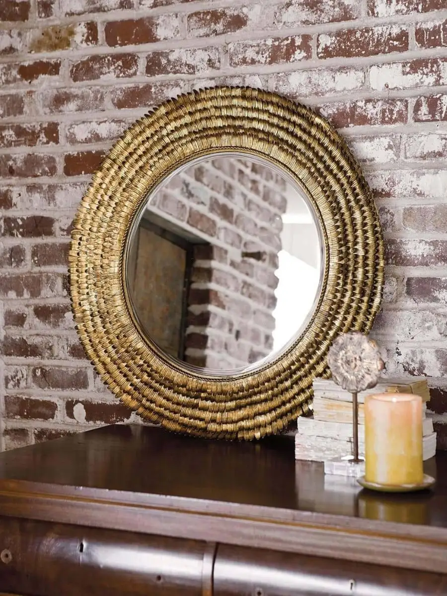 Old Money Home Decor: Easy Styling Steps to Make an Average Room Look High-End Round scalloped gold mirror resting on a dark wood console table next to a pillar candle. Warm metallic centerpiece anchor to reflect natural light in a living room layout.