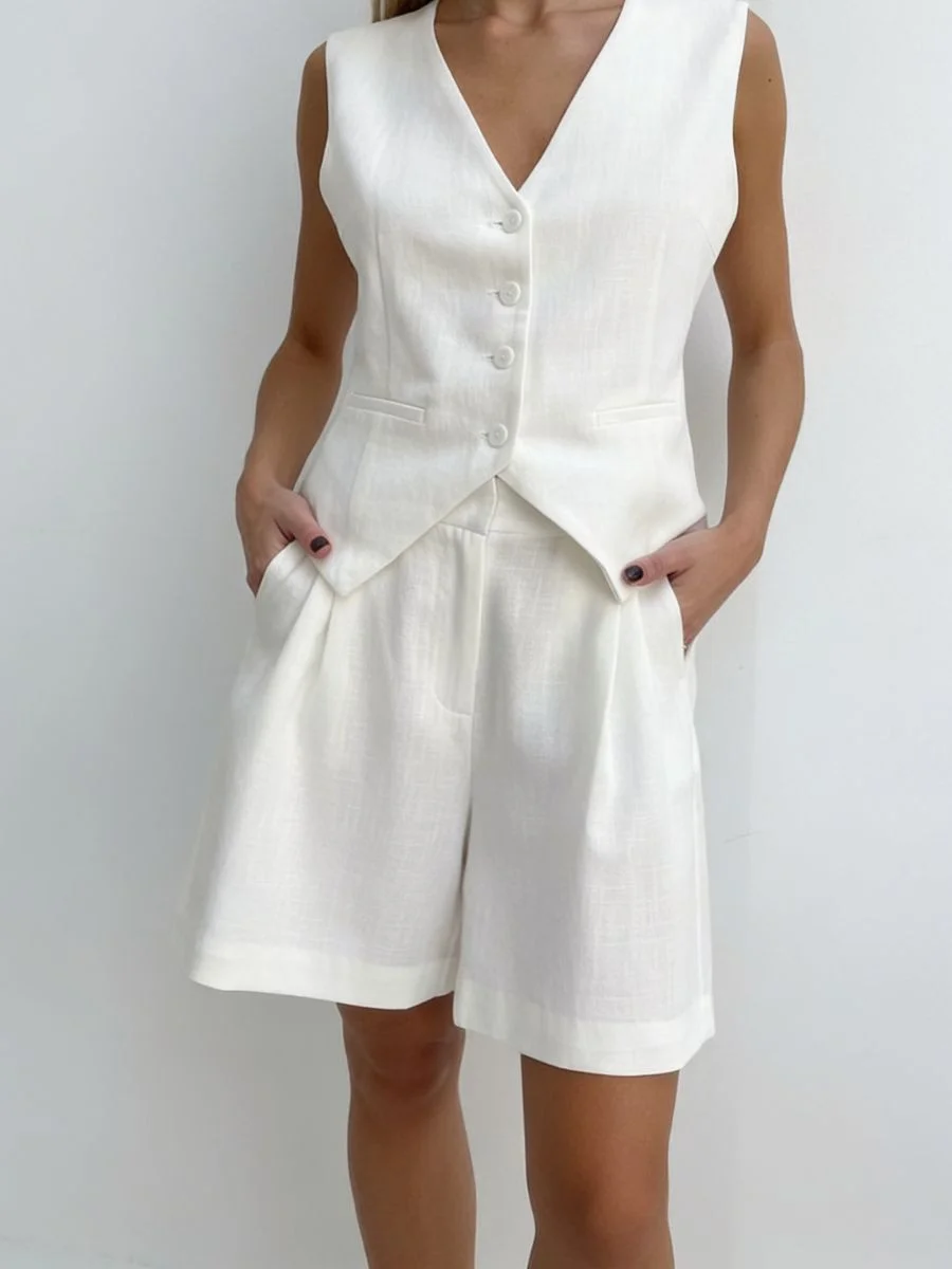 Studio lookbook view of an all white linen suit vest and shorts set showing the pointed front hem of the vest overlapping the waist.