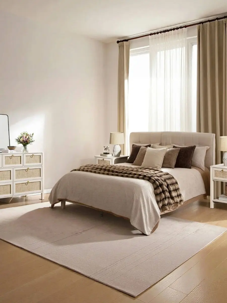 A wide bedroom shot displaying a white cream oak cane nightstand sitting flush with a tall mattress next to a matching 7-drawer dresser with gold handles.