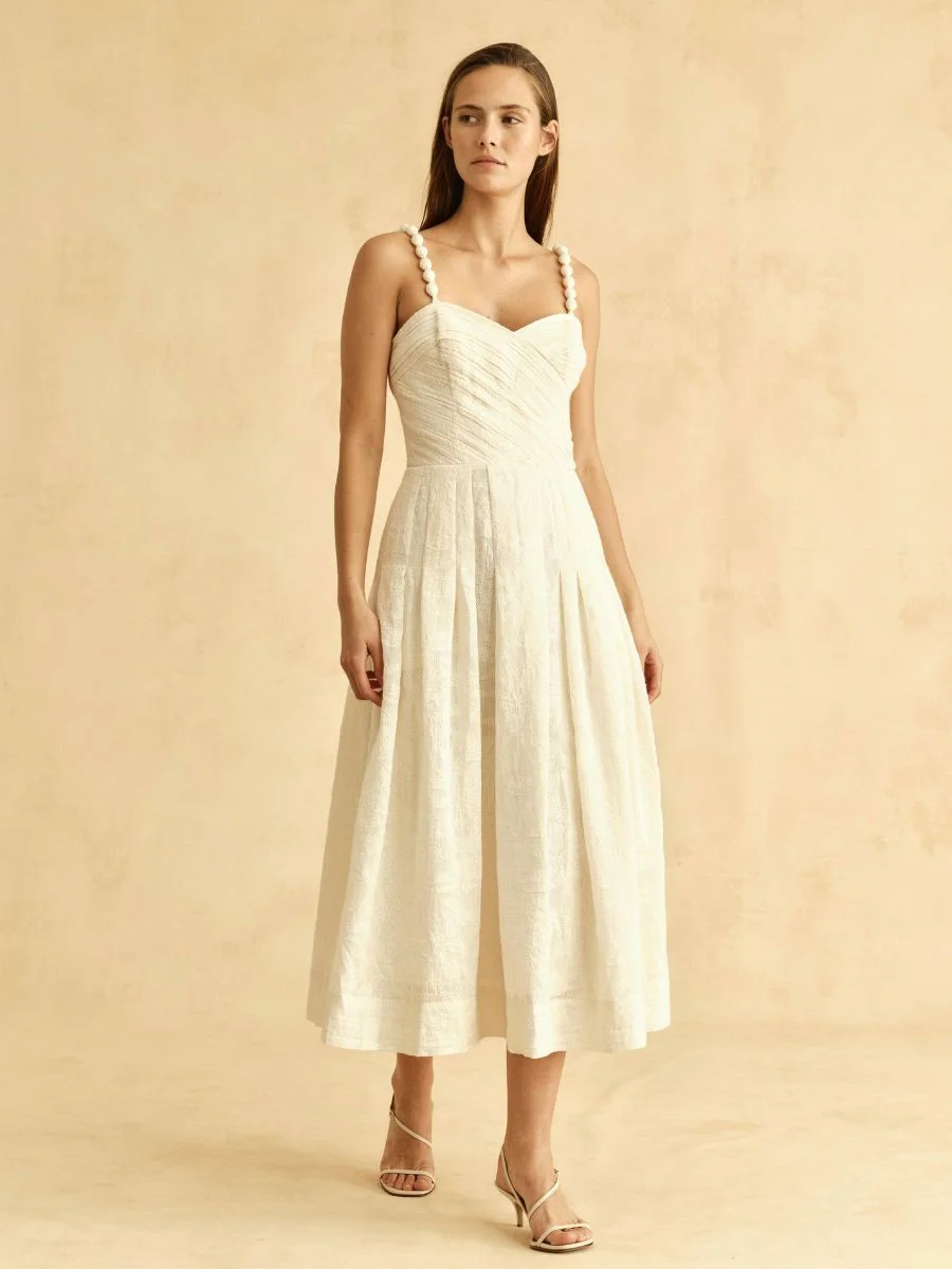 A woman poses on a beige background wearing the ivory Cartolina Marabel woven jacquard midi dress with a sweetheart neckline and beaded straps.