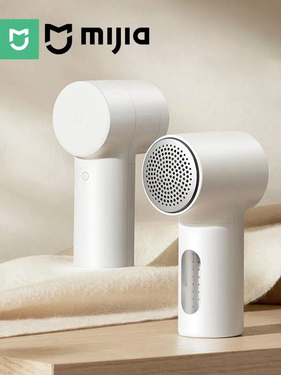 Two white minimalist Xiaomi Mijia fabric lint shavers resting on a light wooden table next to a folded soft neutral cashmere wool blanket.
