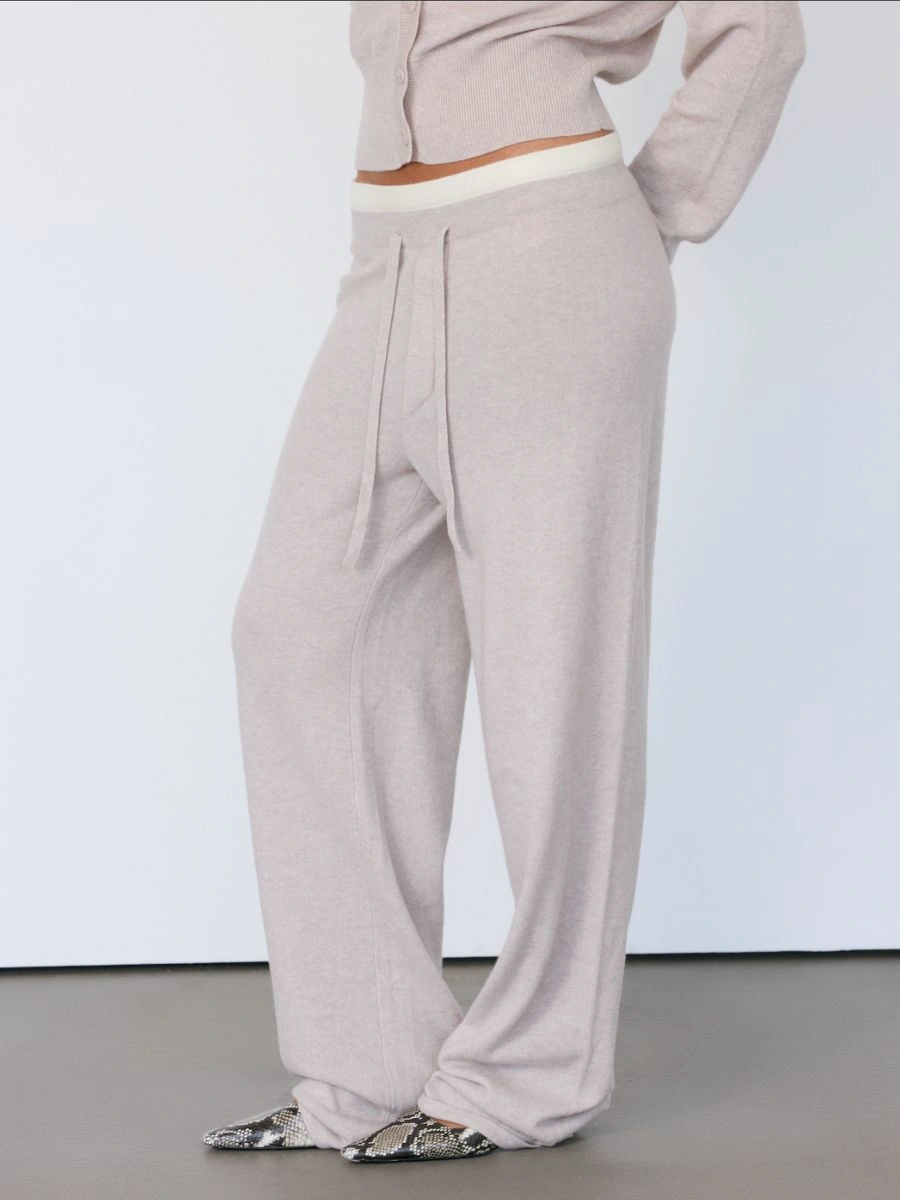 Close up view of the beige Artless Tove knit lounge trousers pooling over snakeskin patterned leather boots.