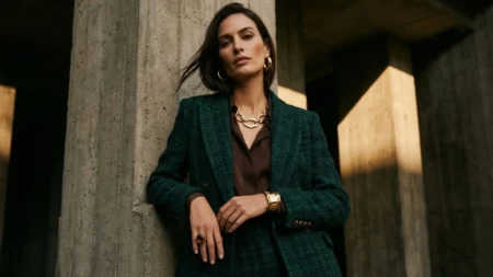 Confident woman wearing a structured forest green tweed fall blazer accessorized with bold gold jewelry.