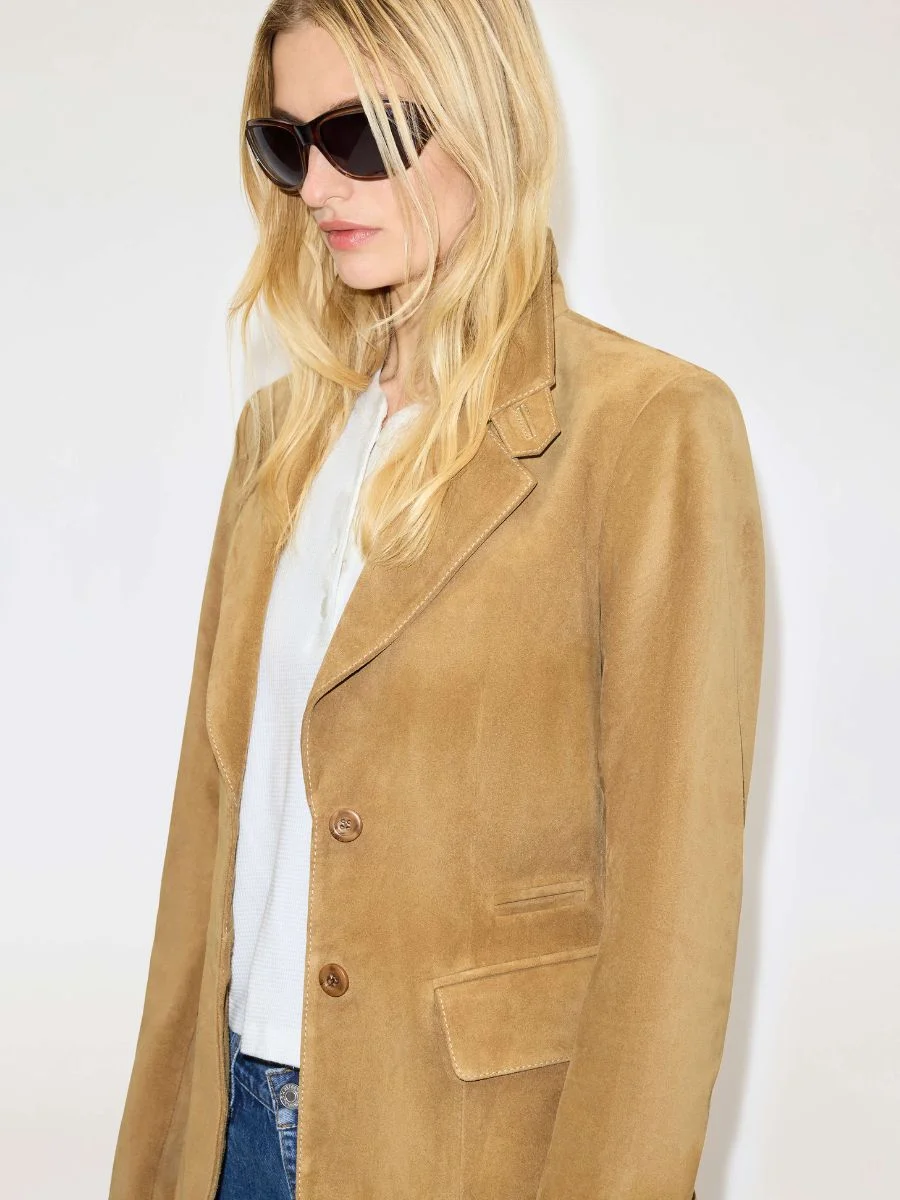 Model wearing a fitted, tobacco-colored RE/DONE calf suede blazer with structured shoulders and dark sunglasses.
