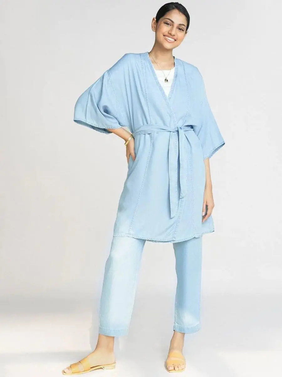 Woman wearing a light blue Tencel duster jacket tied with a matching fabric belt over matching relaxed pants.