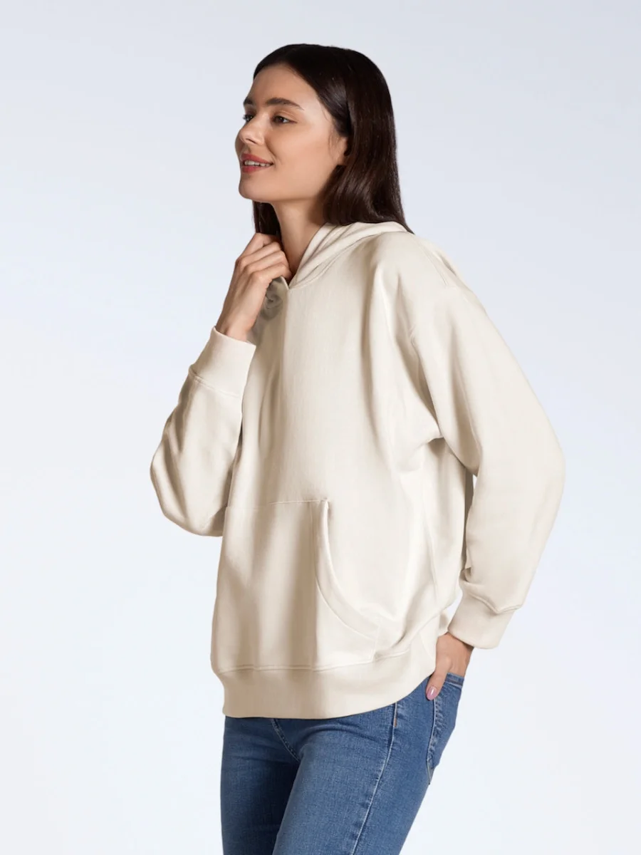 Side view of a woman wearing a heavy cream-colored oversized organic cotton hoodie with blue jeans.
