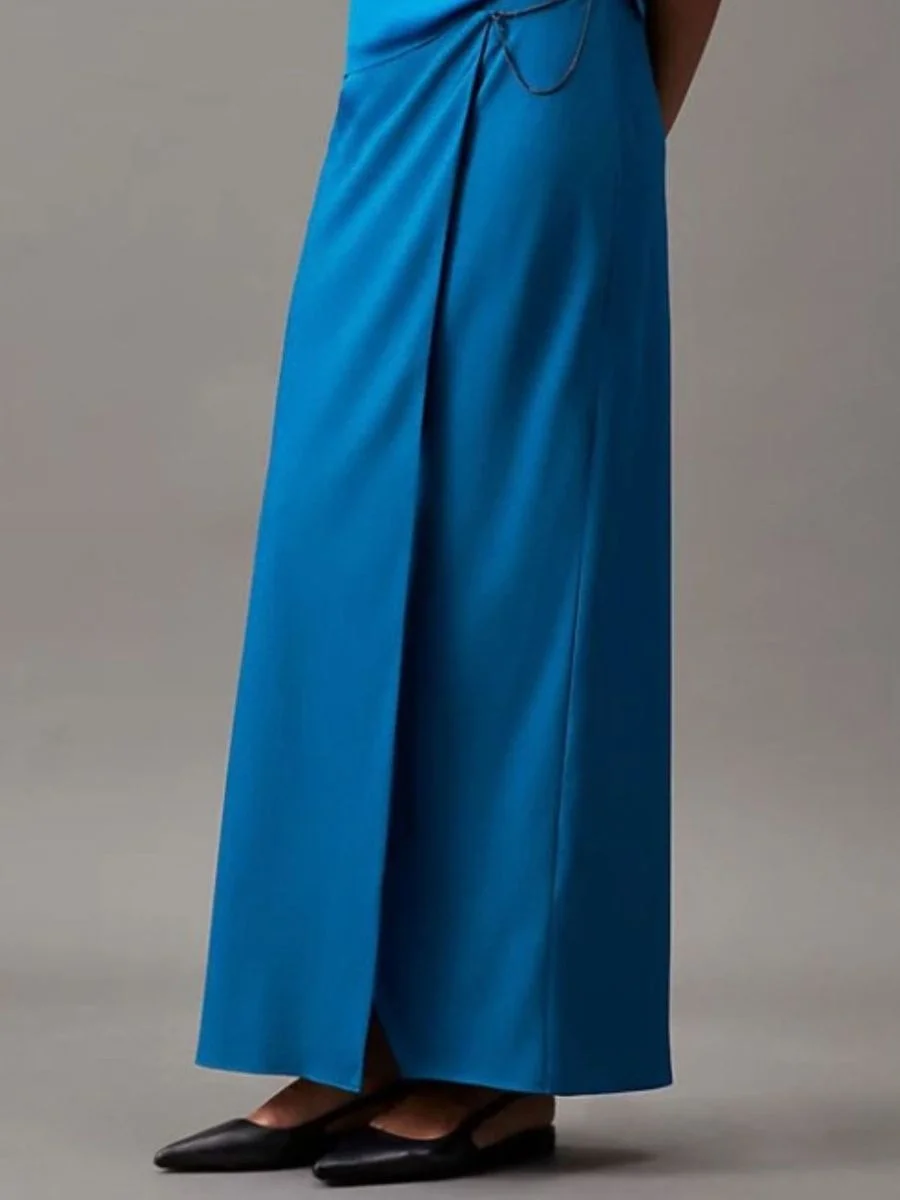 Calvin Klein wrap-style maxi skirt in a rich blue matte crepe de chine fabric, featuring a subtle metal chain detail at the waist and a comfortable viscose lining, paired with black pointed flat shoes.