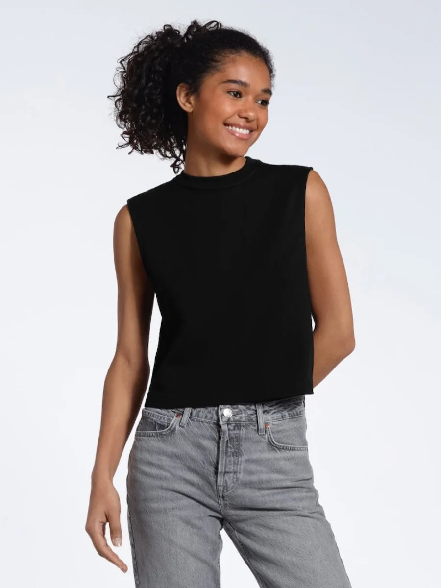 A woman modeling a structured black ribbed knit tank top from Plain and Simple styled with high-waisted grey denim jeans.