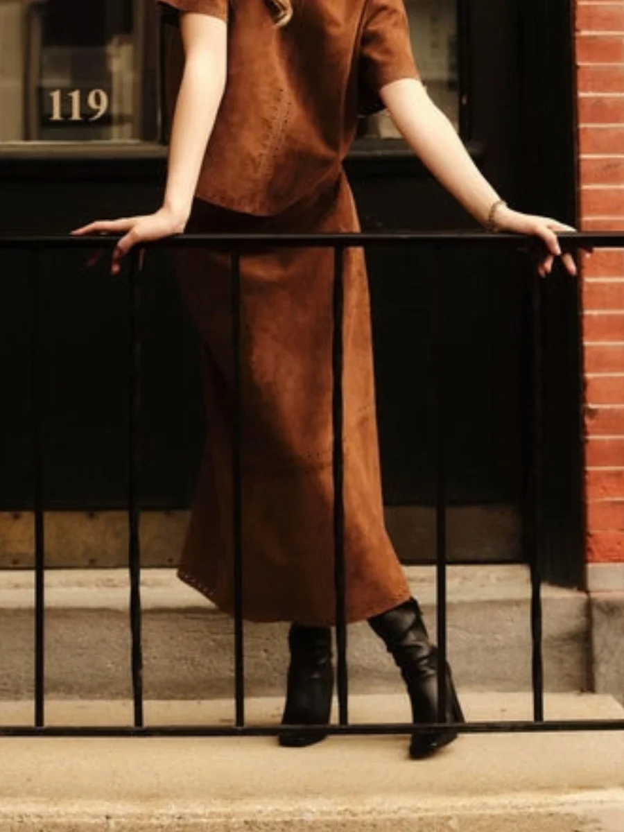 A monochrome chestnut look from Cartolina showing what is a capsule wardrobe, featuring their brown suede A-line midi skirt and matching short-sleeve top styled with black leather boots.